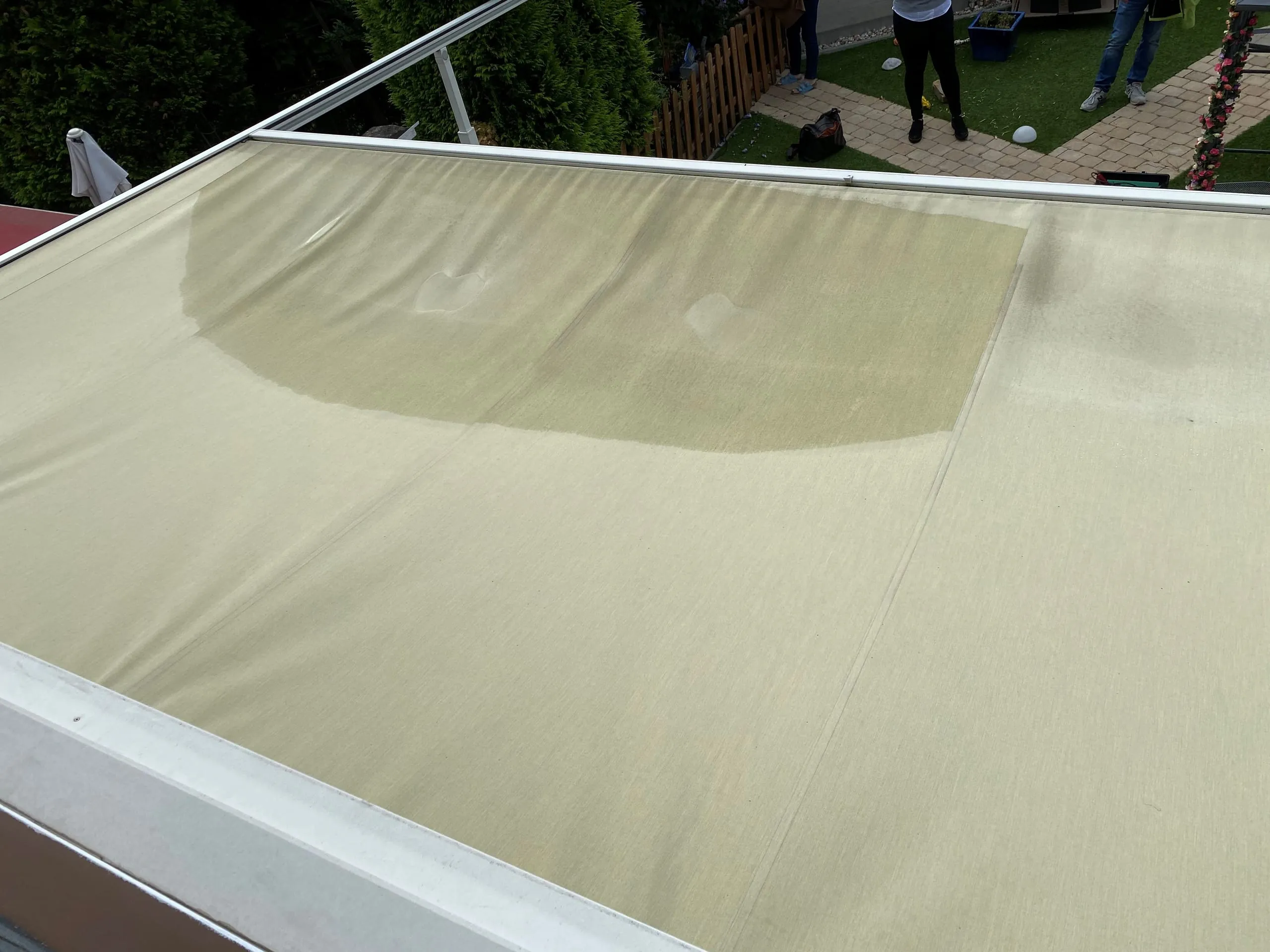 Blick von oben auf das Markisentuch: Wo der Wassersack war, ist nun ein nasser, ausgebeulter Bereich sichtbar. Die Imprägnierung ist dort nahezu nicht mehr vorhanden. Rechts sind weitere, bereits ältere Schmutzspuren zu erkennen.