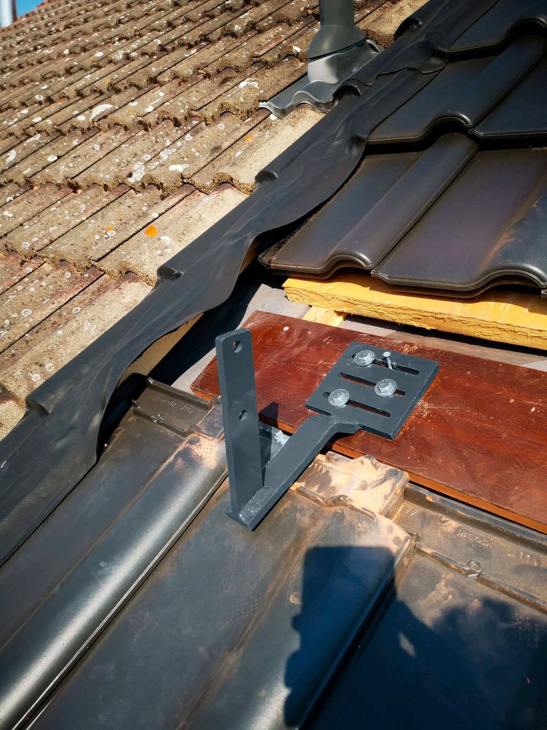 Heben Sie zunächst eine Reihe an Dachziegeln aus und schrauben Sie je einen Dachhalter per Wasserwaage auf den ersten und letzten Sparren. Die Langlöcher erlauben Korrekturen in der Ausrichtung.