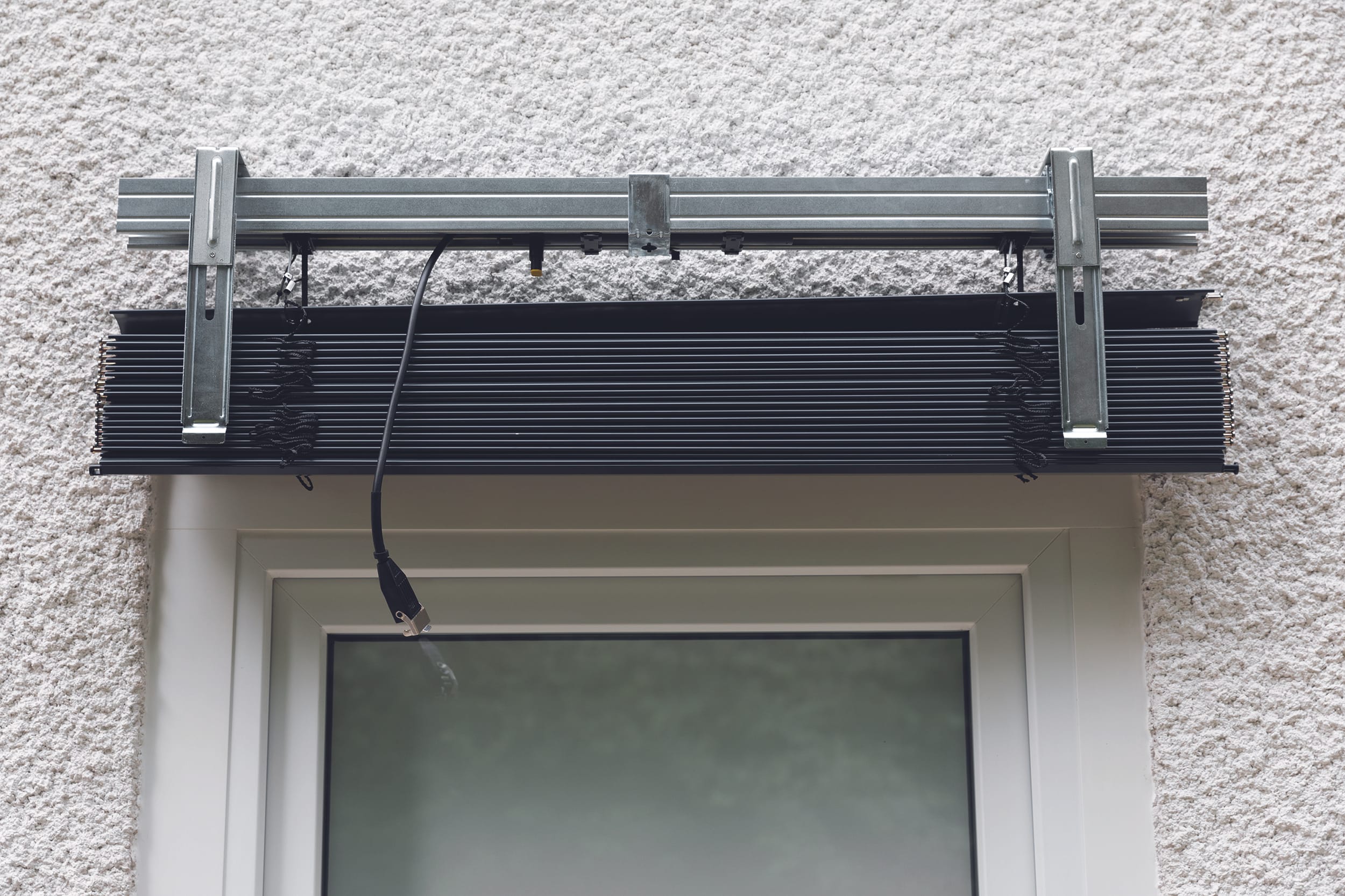 Lösen Sie auf beiden Seiten den Federmechanismus und öffnen Sie den Rasthalter. Hängen Sie das Raffstore-Paket ein und richten Sie es mittig aus.