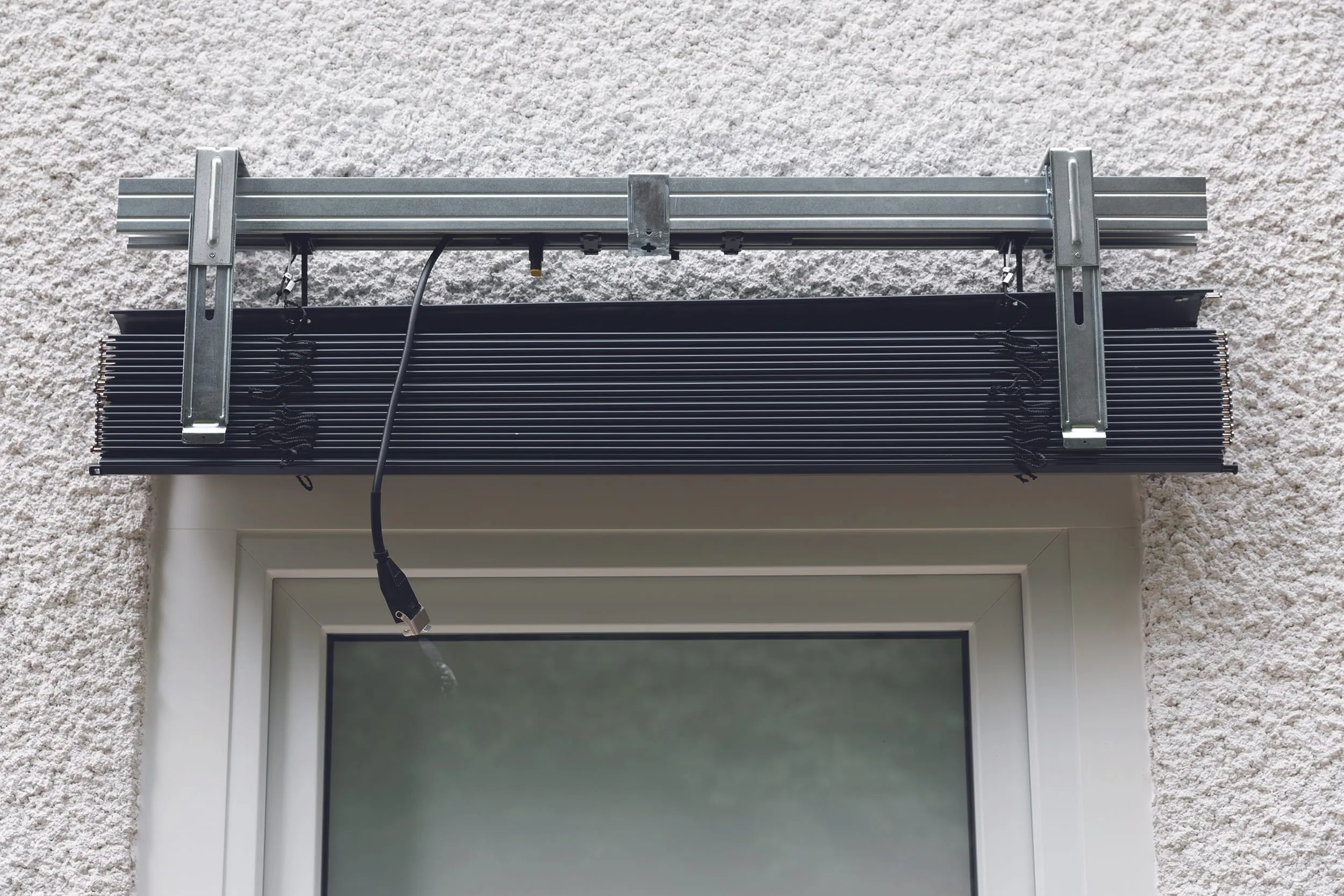 Lösen Sie auf beiden Seiten den Federmechanismus und öffnen Sie den Rasthalter. Hängen Sie das Raffstore-Paket ein und richten Sie es mittig aus.