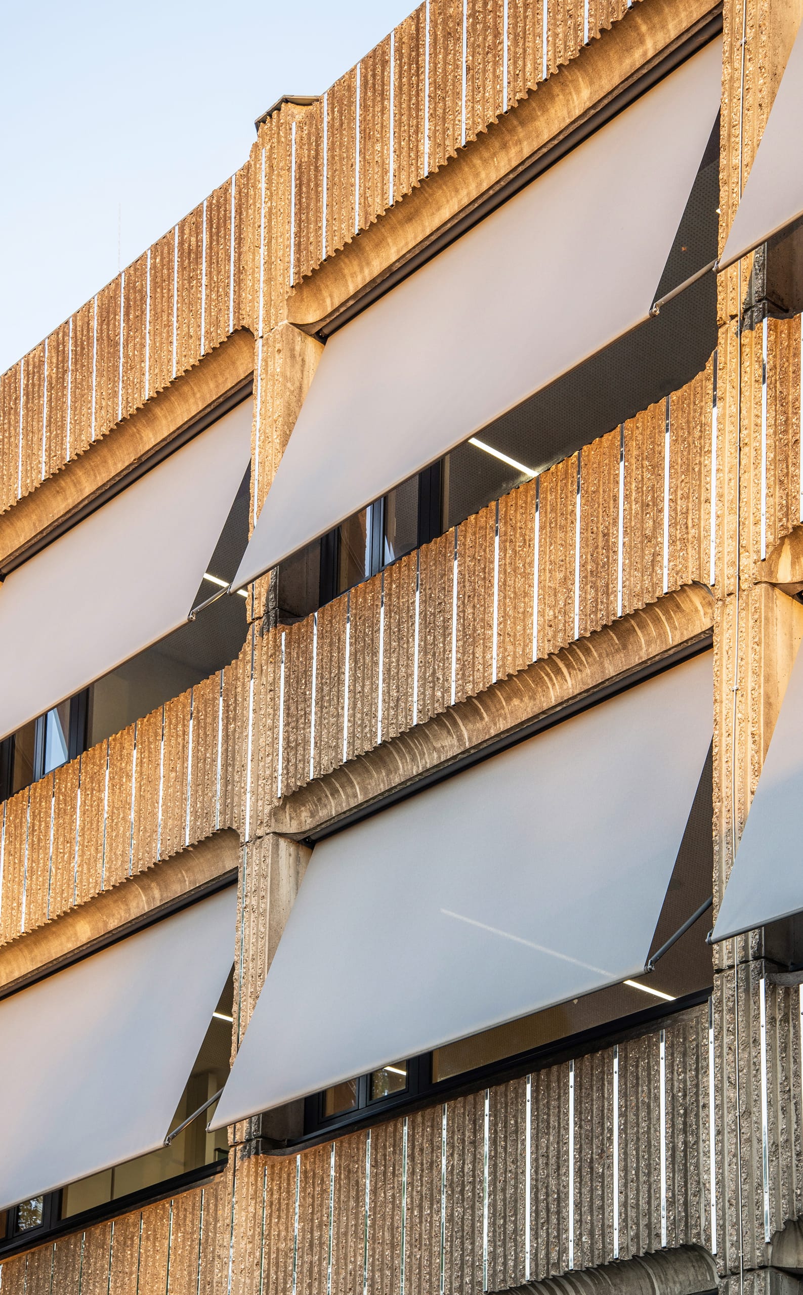Vertikale Aluminiumleisten nehmen der Betonarchitektur die Schwere und lockern die strenge Struktur der Fassade auf. Die alten Fenster wurden ausgetauscht und die neuen Holzfenster mit Warema Fallarm-Markisen als Sonnen- und Blendschutz geschützt.