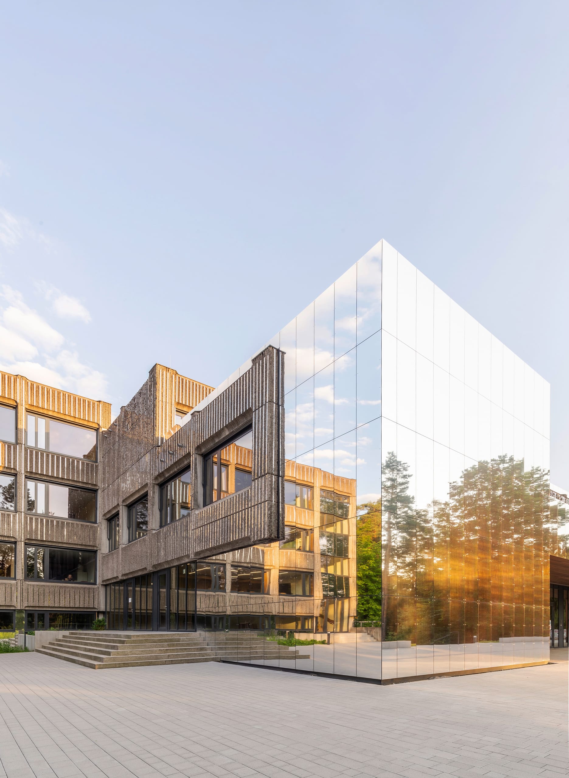 Eine spiegelnde Aluminium-Fassade kontrastiert die Beton-brut-Architektur des Bestandsbaus und ergänzt die alte Betonfertigteil-Fassade da, wo Neues gebaut wurde.