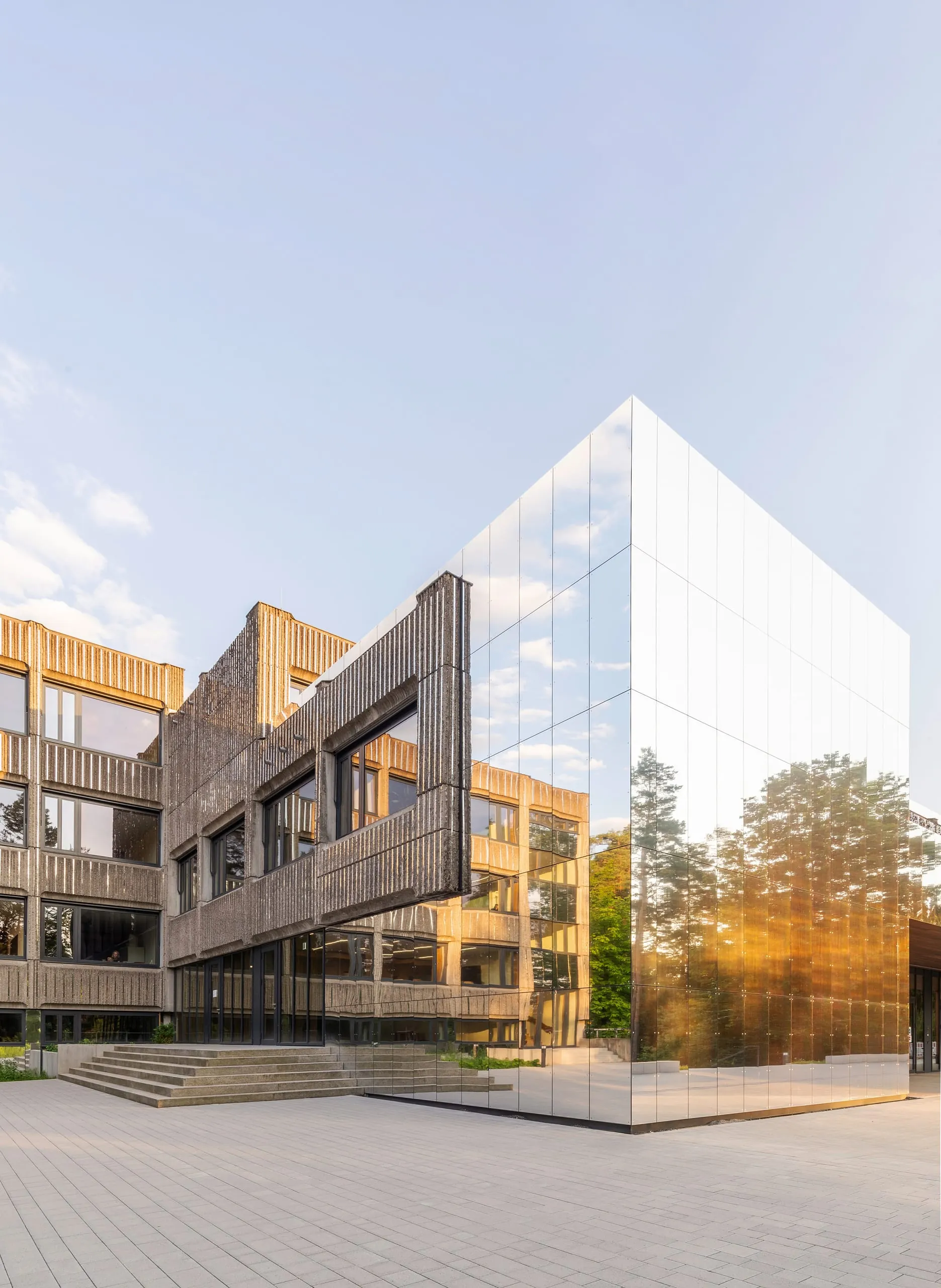 Eine spiegelnde Aluminium-Fassade kontrastiert die Beton-brut-Architektur des Bestandsbaus und ergänzt die alte Betonfertigteil-Fassade da, wo Neues gebaut wurde.