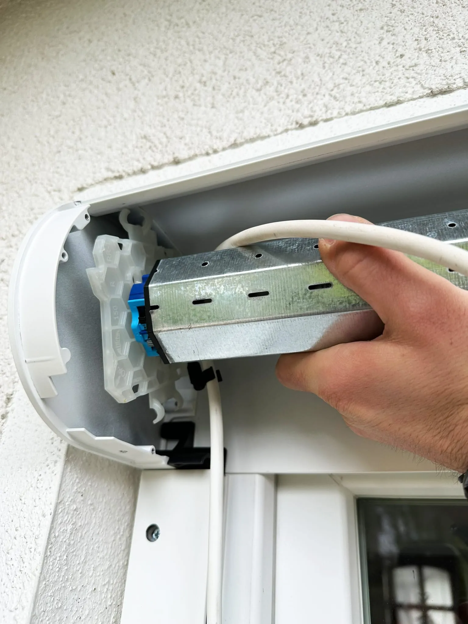 Setzen Sie den Antrieb in korrekter Position in den Kasten ein. Achten Sie darauf, dass alle Komponenten fest und sicher sitzen und Anschlussleitung sowie Antenne so verlegt sind, dass sie in keinem Fall in den Verfahrweg des Behangs geraten. Denken Sie bei der Leitungsverlegung auch an die Abtropfschleife im Kasten.