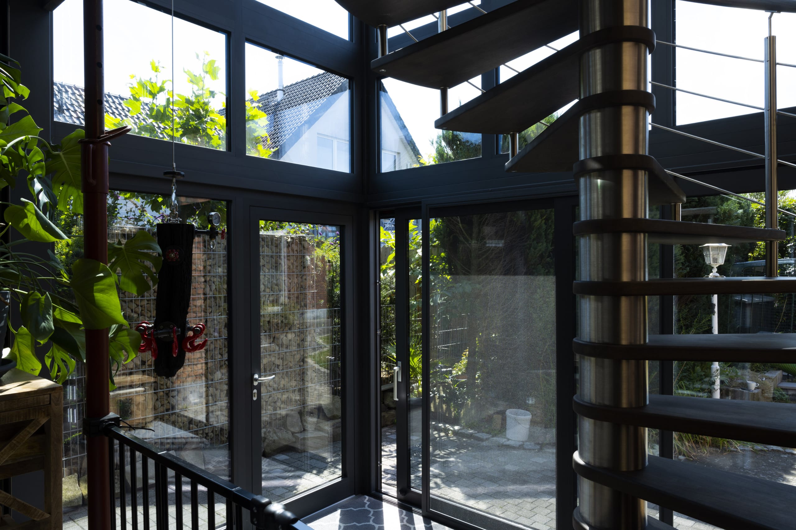 Der Raum im Erdgeschoss dient als Wohnzimmer mit direktem Zugang zum Garten – inklusive zweiflügeliger Hebe-Schiebetür. Die kompakte Wendeltreppe führt direkt an der Glasfassade entlang, wie ein offenes Treppenhaus und dennoch wettergeschützt, mitten im Wohnraum. Für entspannende Abendstunden verfügt der Wintergarten über ein harmonisches Beleuchtungs-Konzept.