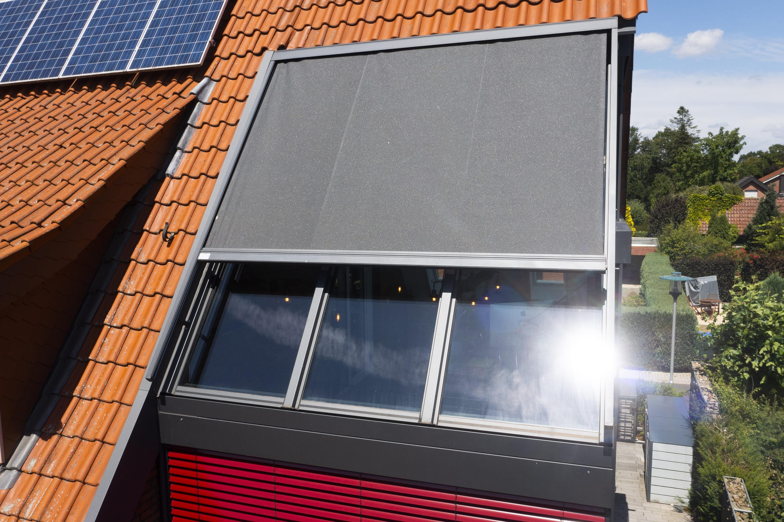 Meint es die Sonne mal zu gut, verschatten optisch ansprechende, rote Alu-Raffstores und eine Überglasmarkise die Glasflächen. Gleichzeitig kühlt eine Split-Klimaanlage die Räume auf eine angenehme Temperatur. In der kalten Jahreszeit ist der Wohnraum im Wintergarten dank Fußbodenheizung und einem hohen Wärmedämmstandard der Gläser ein komfortabler Entspannungsort.