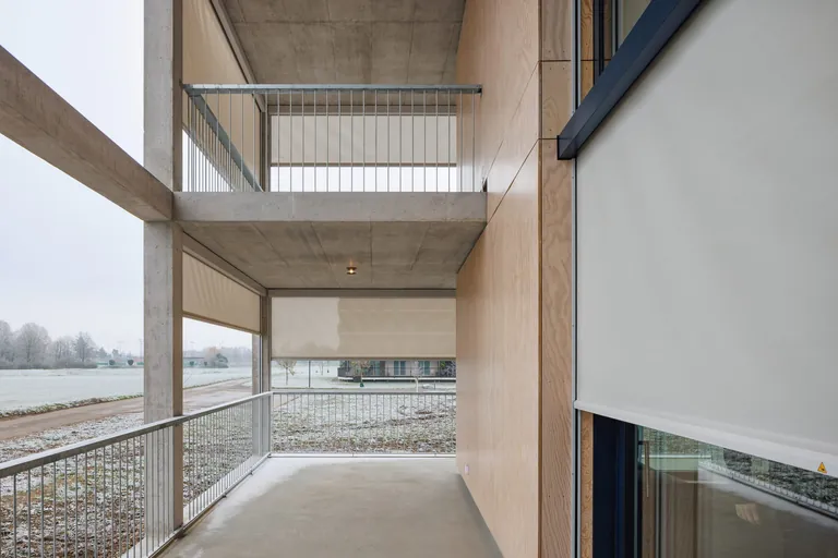 Vor den raumhohen Verglasungen und entlang der umlaufenden Balkone bilden die Zip 6 Senkrechtmarkisen von MHZ eine textile Schicht vor der Fassade.