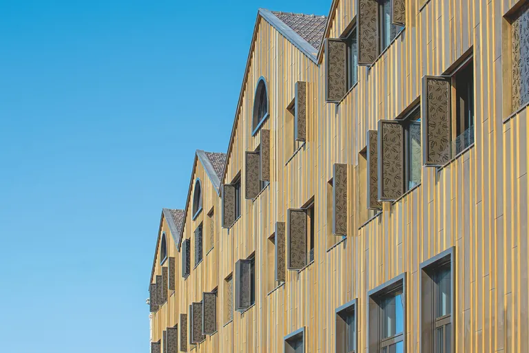 Faltscherenläden mit individuell perforierten Aluminiumfüllungen von Griesser prägen die Fassade des Kornhauses Romanshorn am Bodensee. Die motorisiert gesteuerten Elemente regulieren Tageslicht sowie Blendung und setzen zugleich einen markanten architektonischen Akzent.